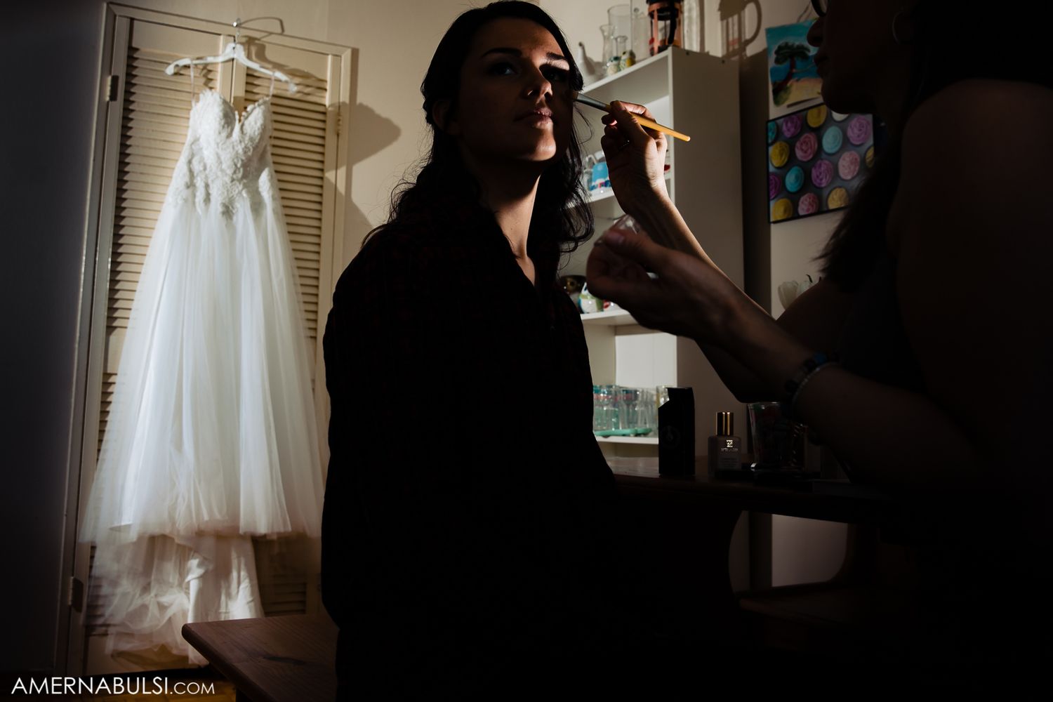 Silhouette of wedding preparation with dress hanging in background.