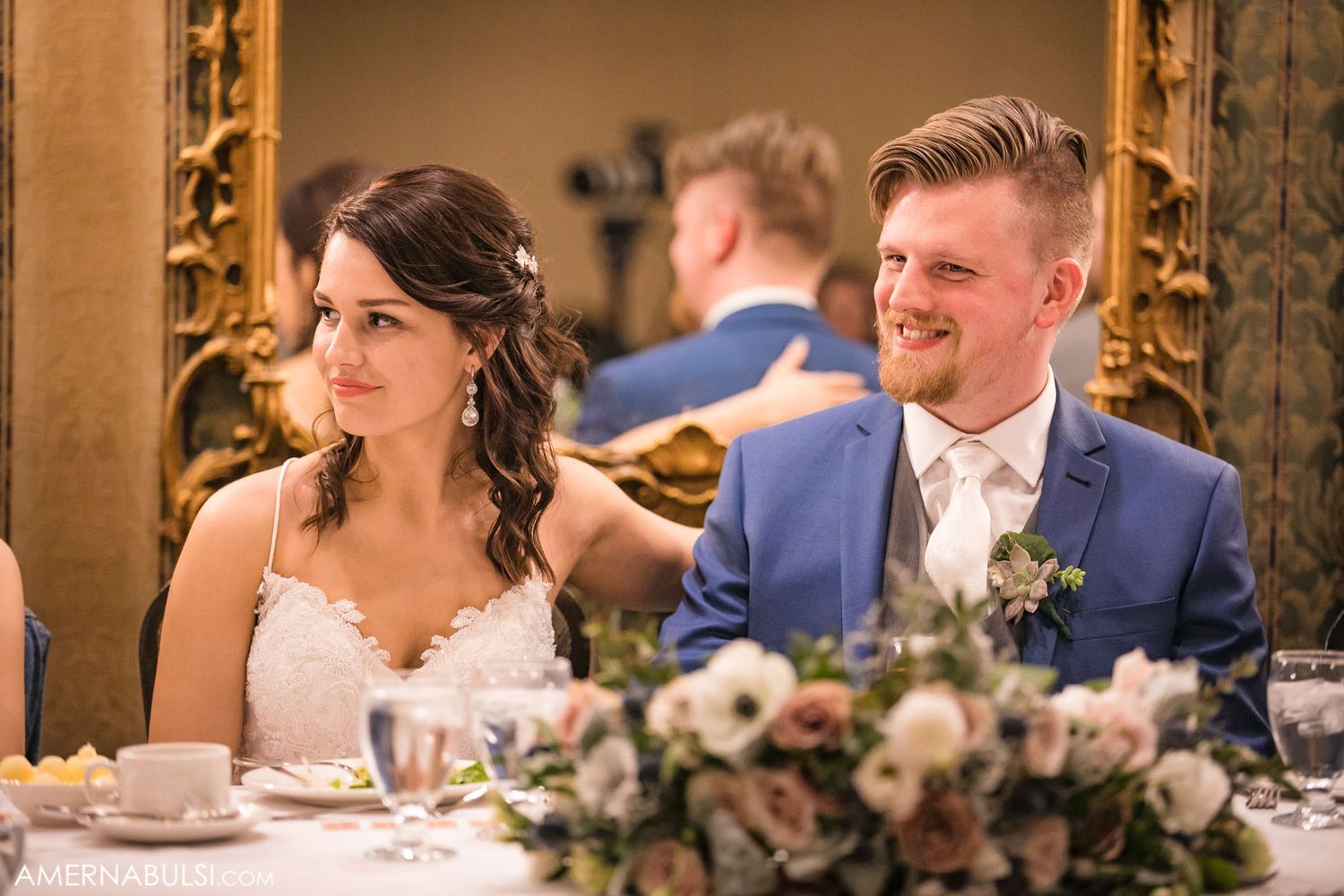 Wedding celebration with guests dining at long tables decorated with floral arrangements and candlelight.