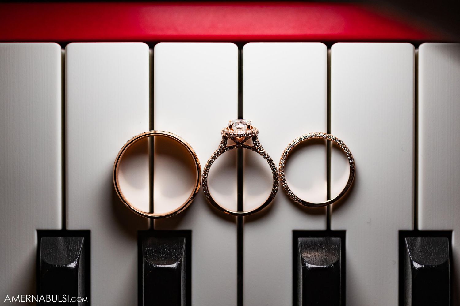 Three wedding rings artistically photographed on a piano keyboard with dramatic lighting.
