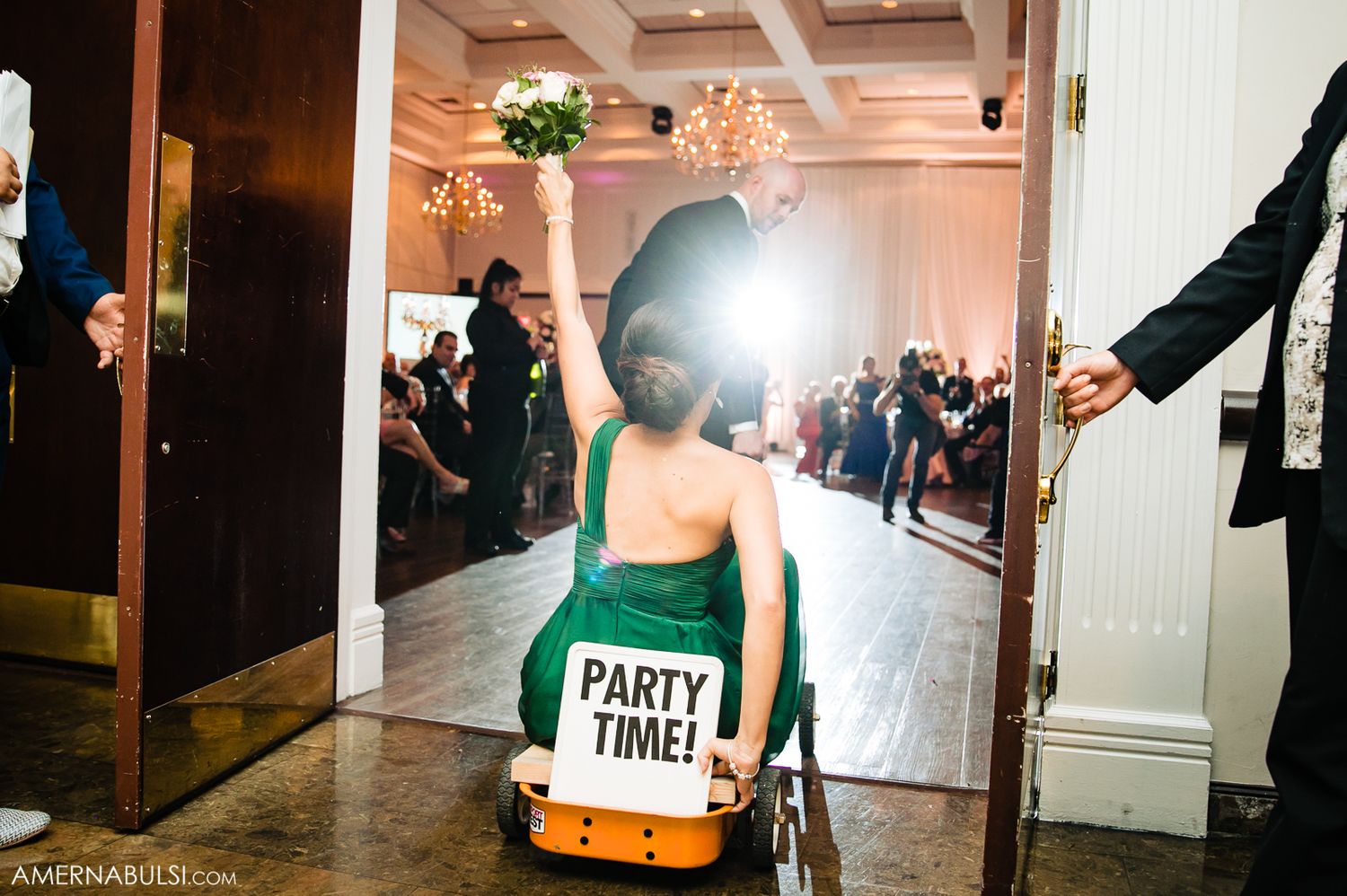 Lively wedding party dancing and celebrating in a dimly lit reception hall with dramatic lighting effects.