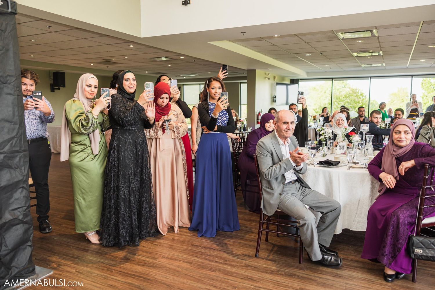 Wedding guests in formal attire and traditional dress gathering for group photos at reception venue.