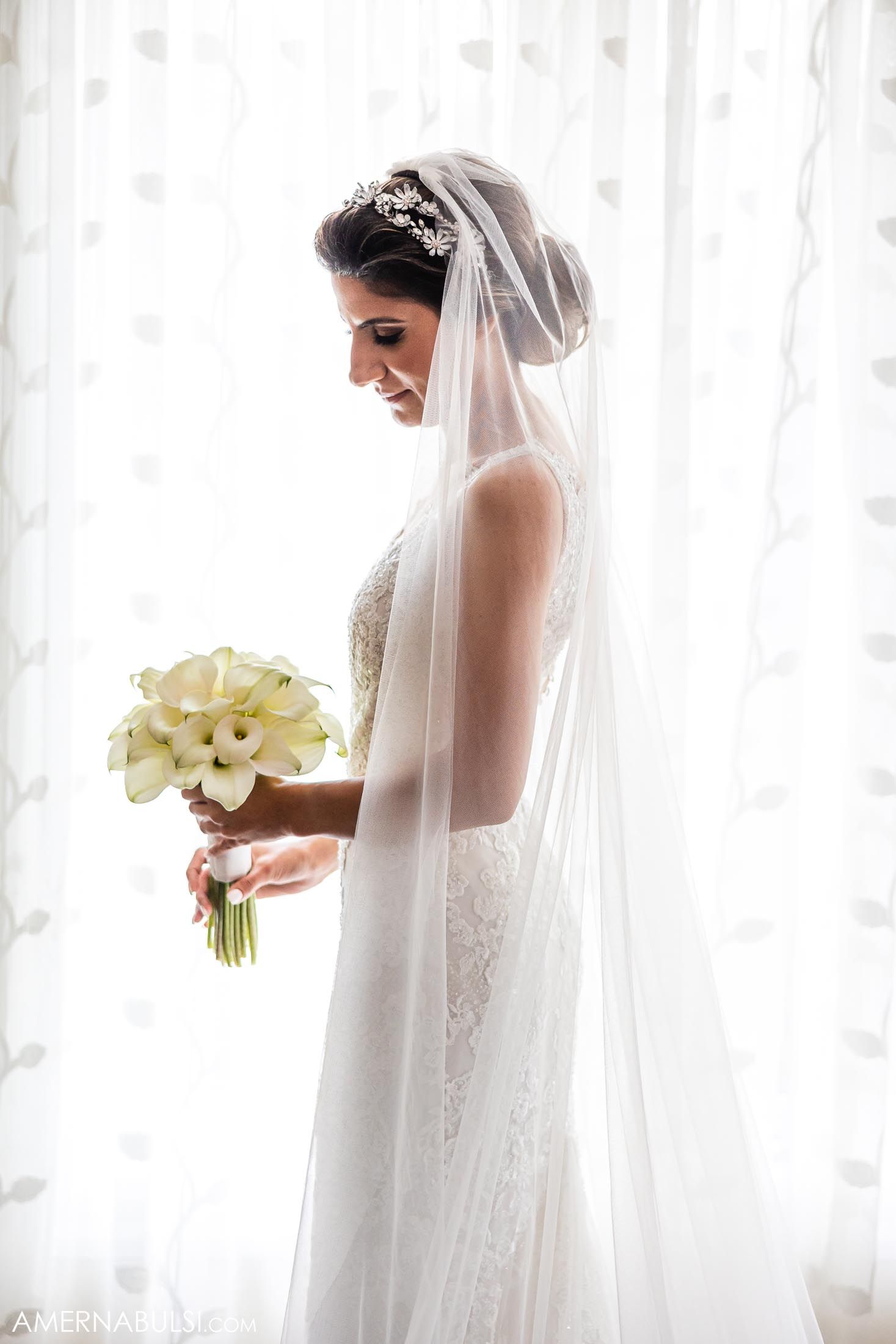Bride in silhouette holding white calla lily bouquet against window light.