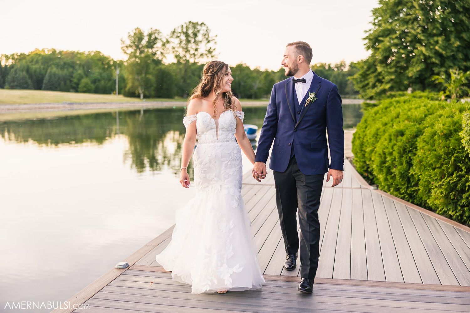 A couple walking hand in hand on a wooden dock by a serene lake.