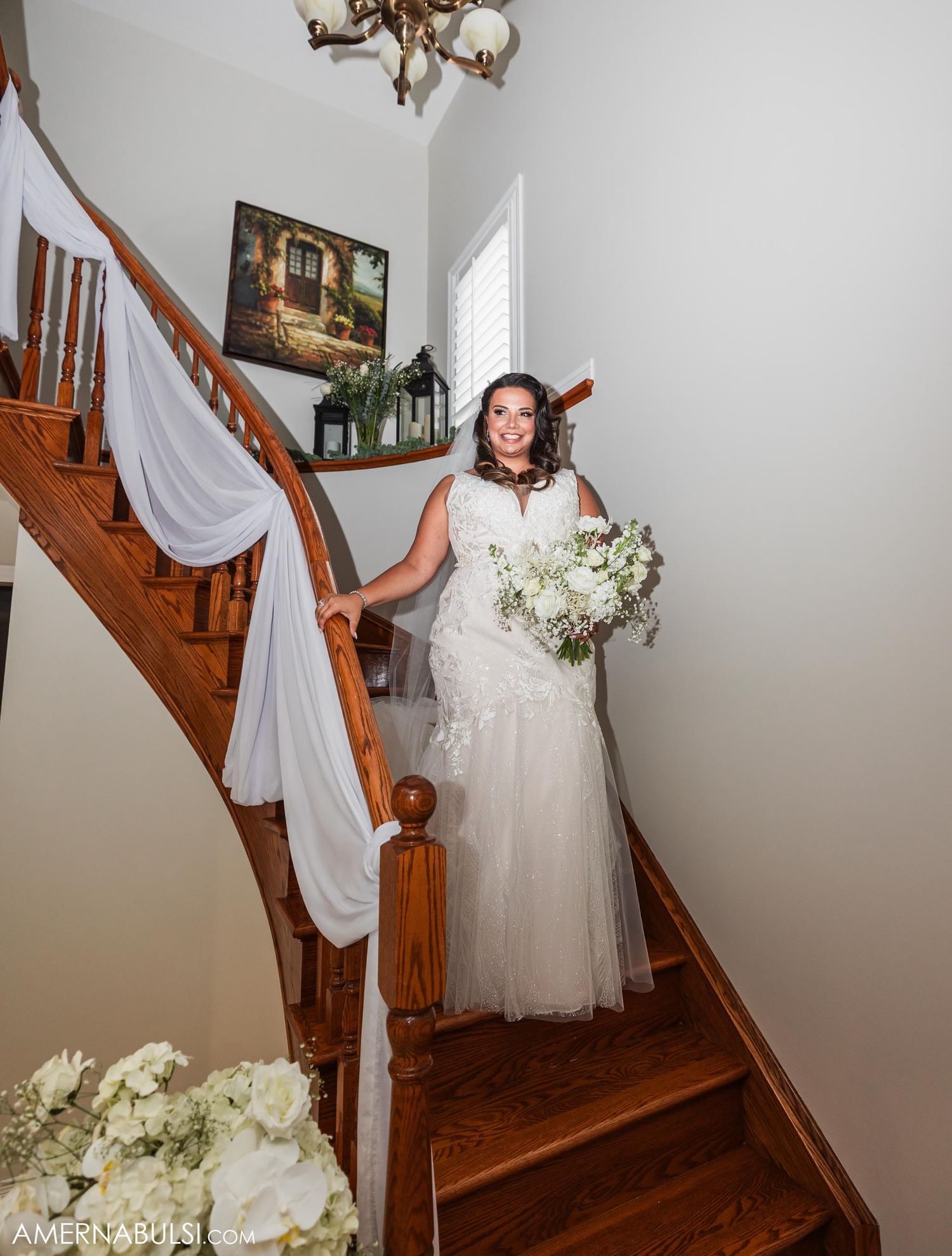 Beautiful white wedding gown with tulle skirt and elegant draping on wooden staircase decorated with white fabric.