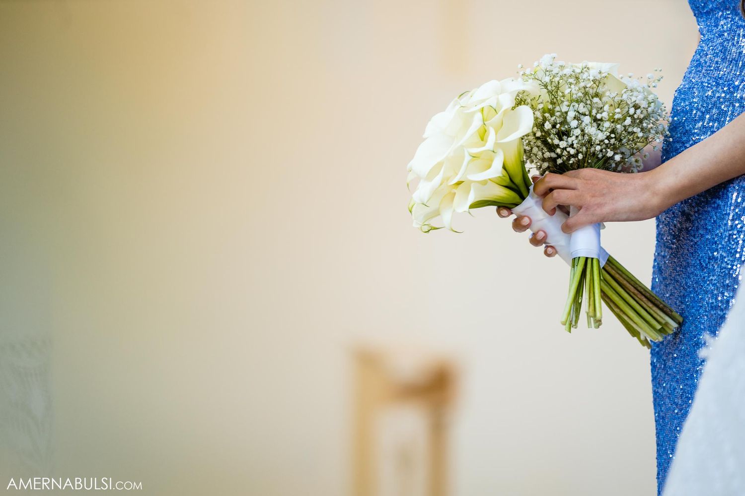White bridal bouquet being held against a blue dress during a wedding ceremony.