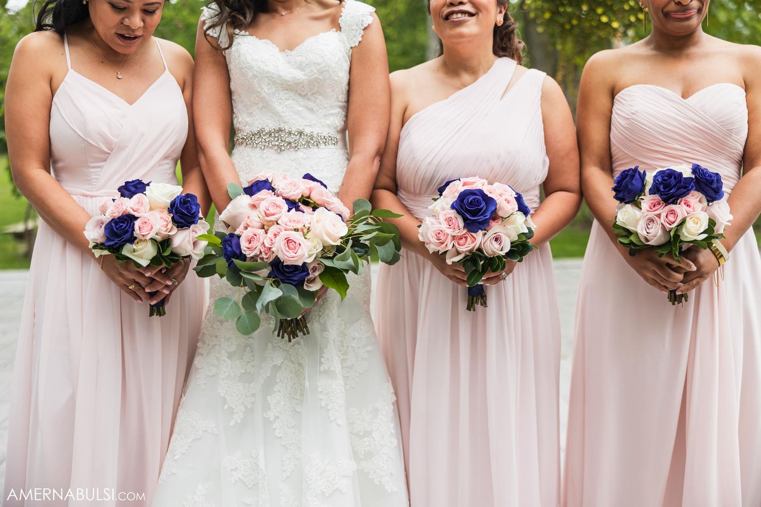 Bridesmaids in blush pink dresses hold matching blue and pink floral bouquets.