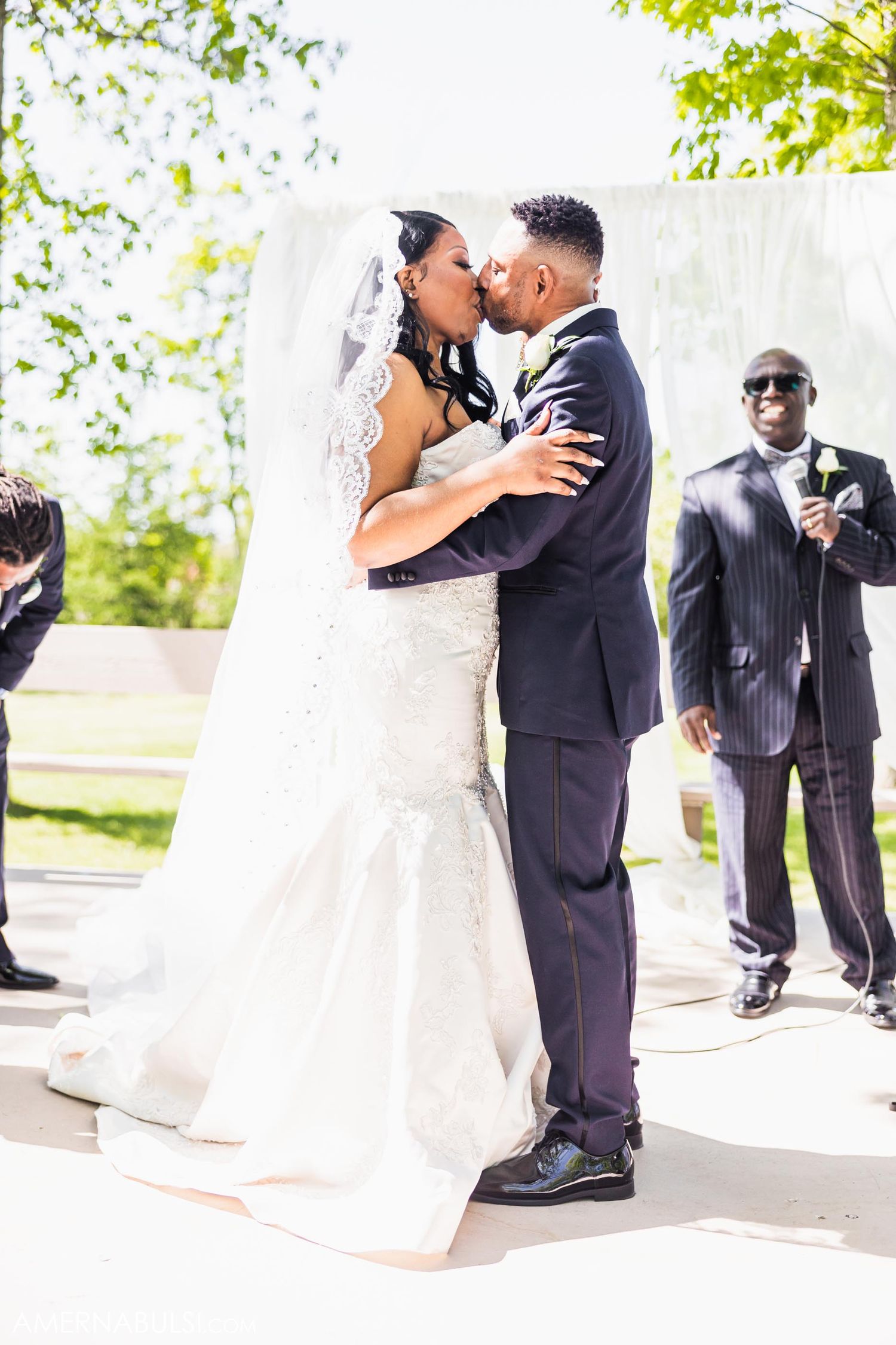 Newlyweds share their first kiss during an outdoor wedding ceremony as guests look on.