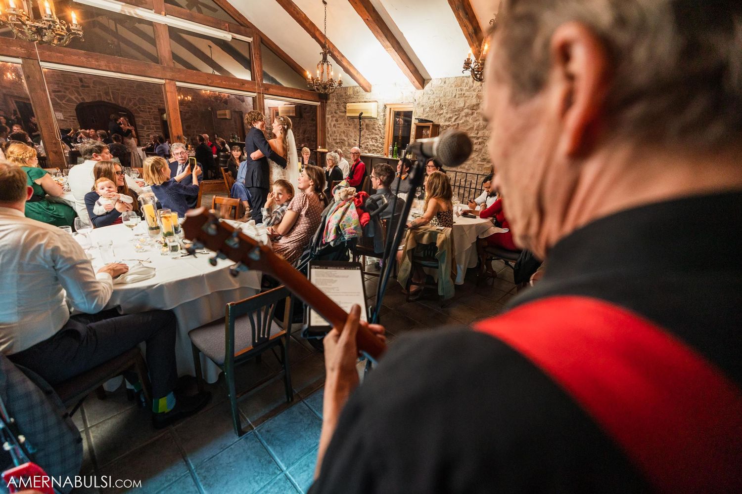 Wedding band performing for reception guests in rustic venue with wooden beams.