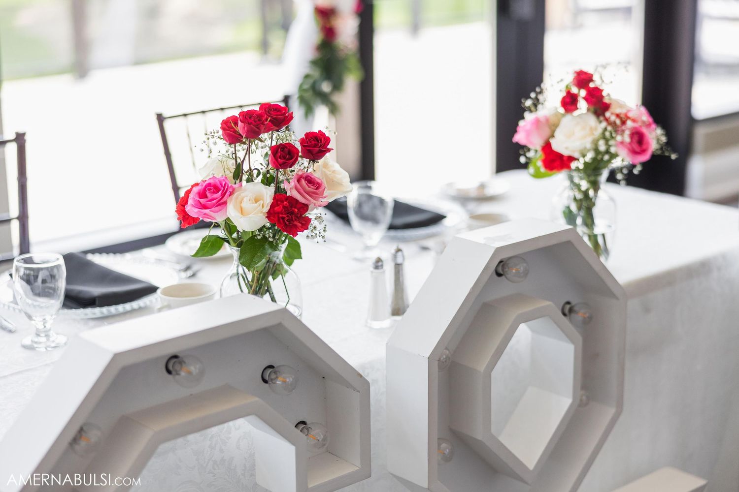 Red and pink roses in glass vases decorate elegant white dining tables.