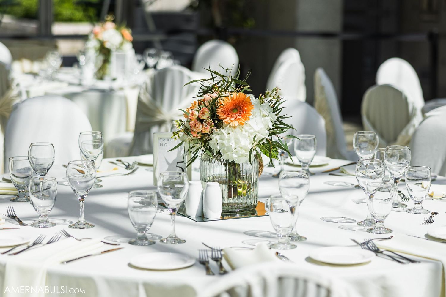 Elegant table setting with white and peach floral centerpiece and crystal glassware.