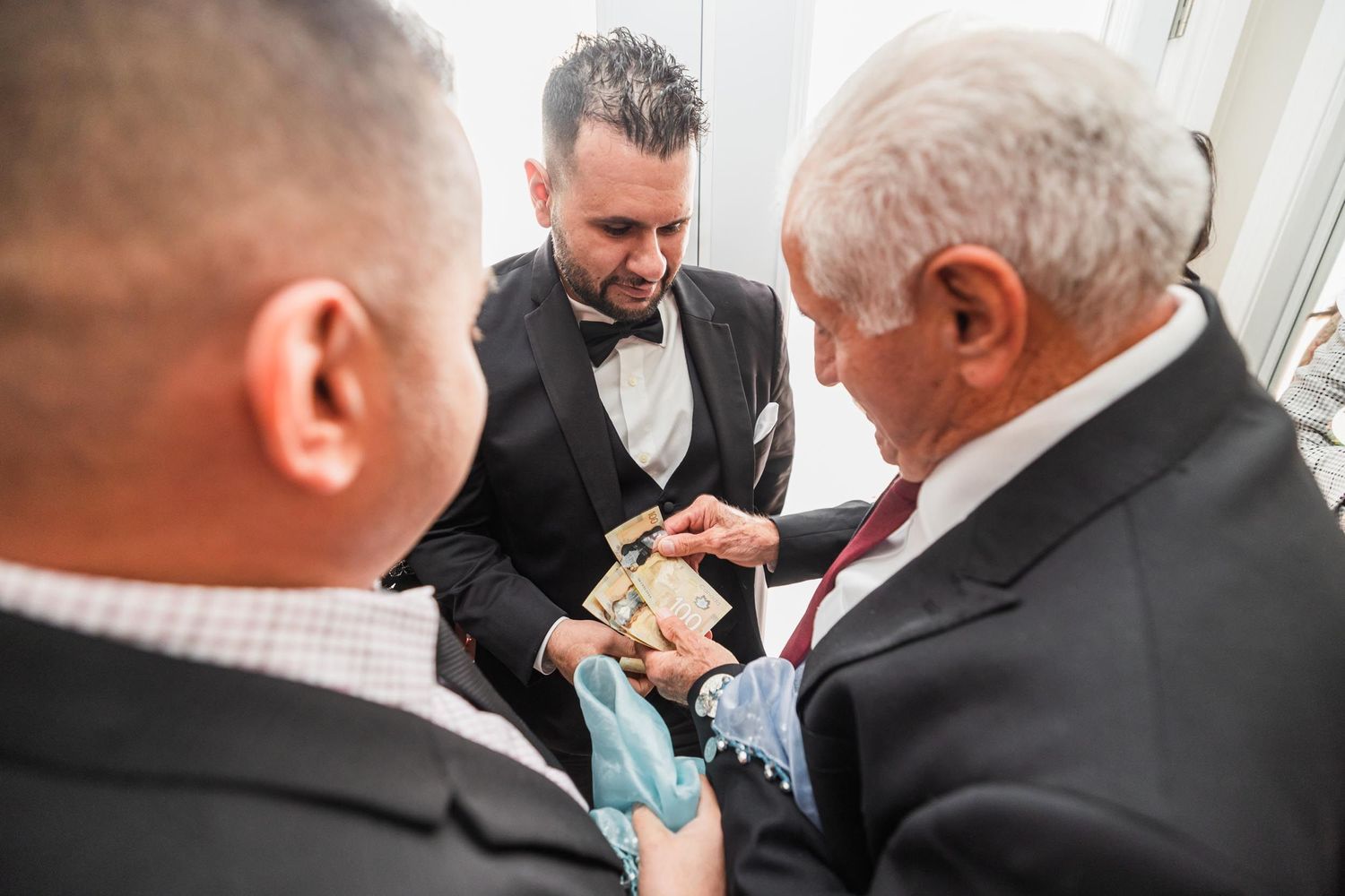 Men in formal attire examine something small during a wedding ceremony.