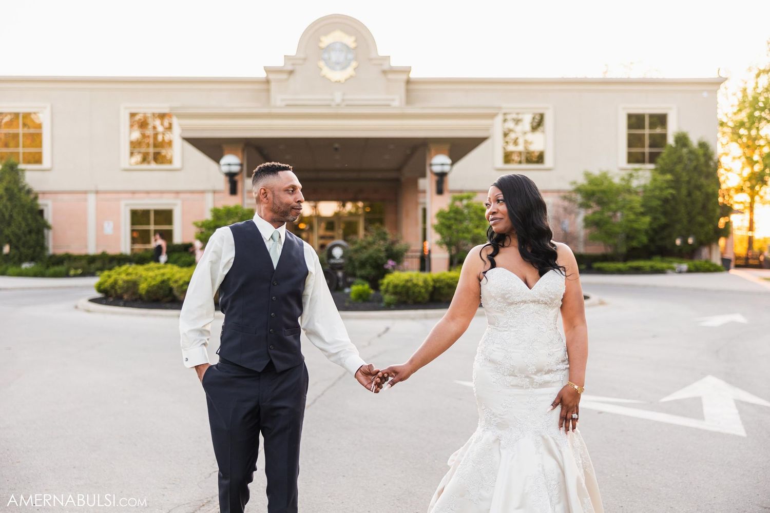Wedding couple holding hands outside an elegant building entrance during their celebration.