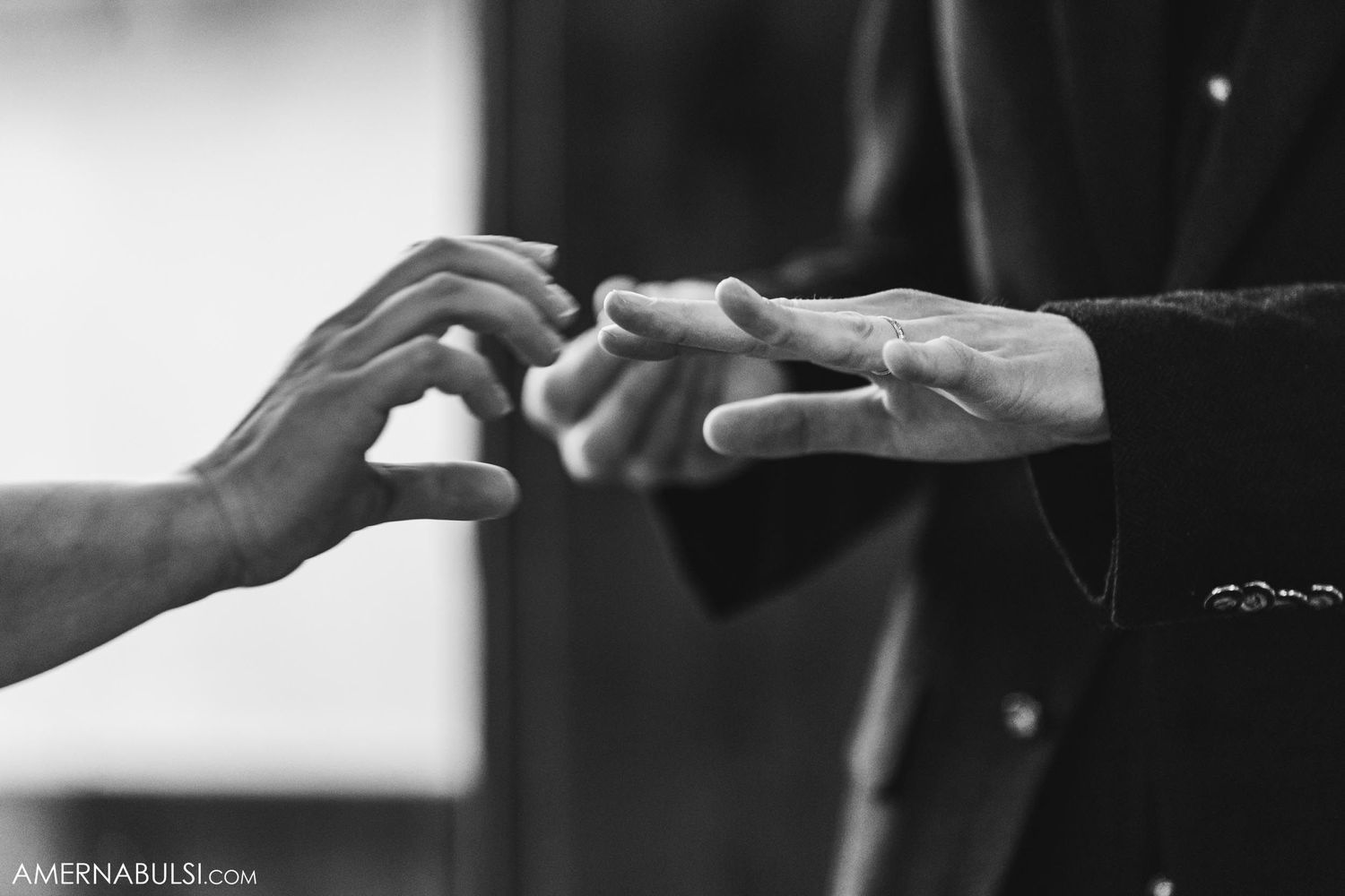 Black and white close-up of hands exchanging wedding rings during ceremony.