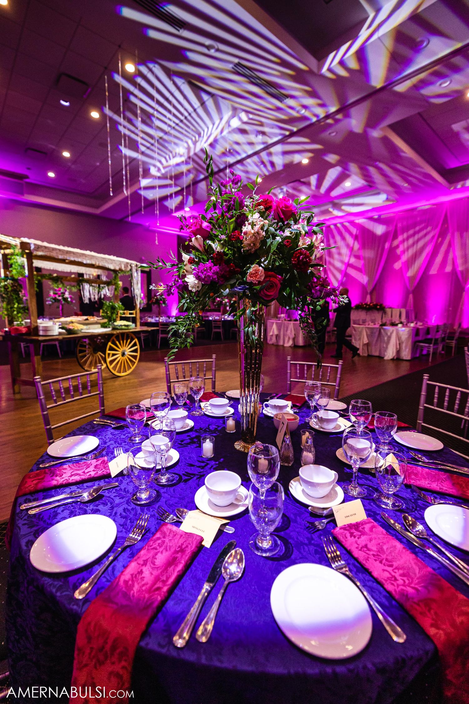 Elegant reception table setting with tall floral centerpiece and purple uplighting creating dramatic patterns.