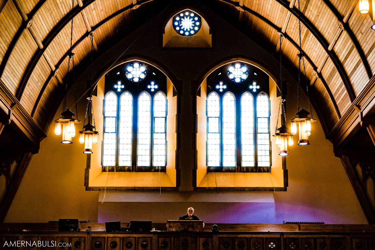 Gothic church interior with vaulted ceiling, stained glass windows and hanging pendant lights.