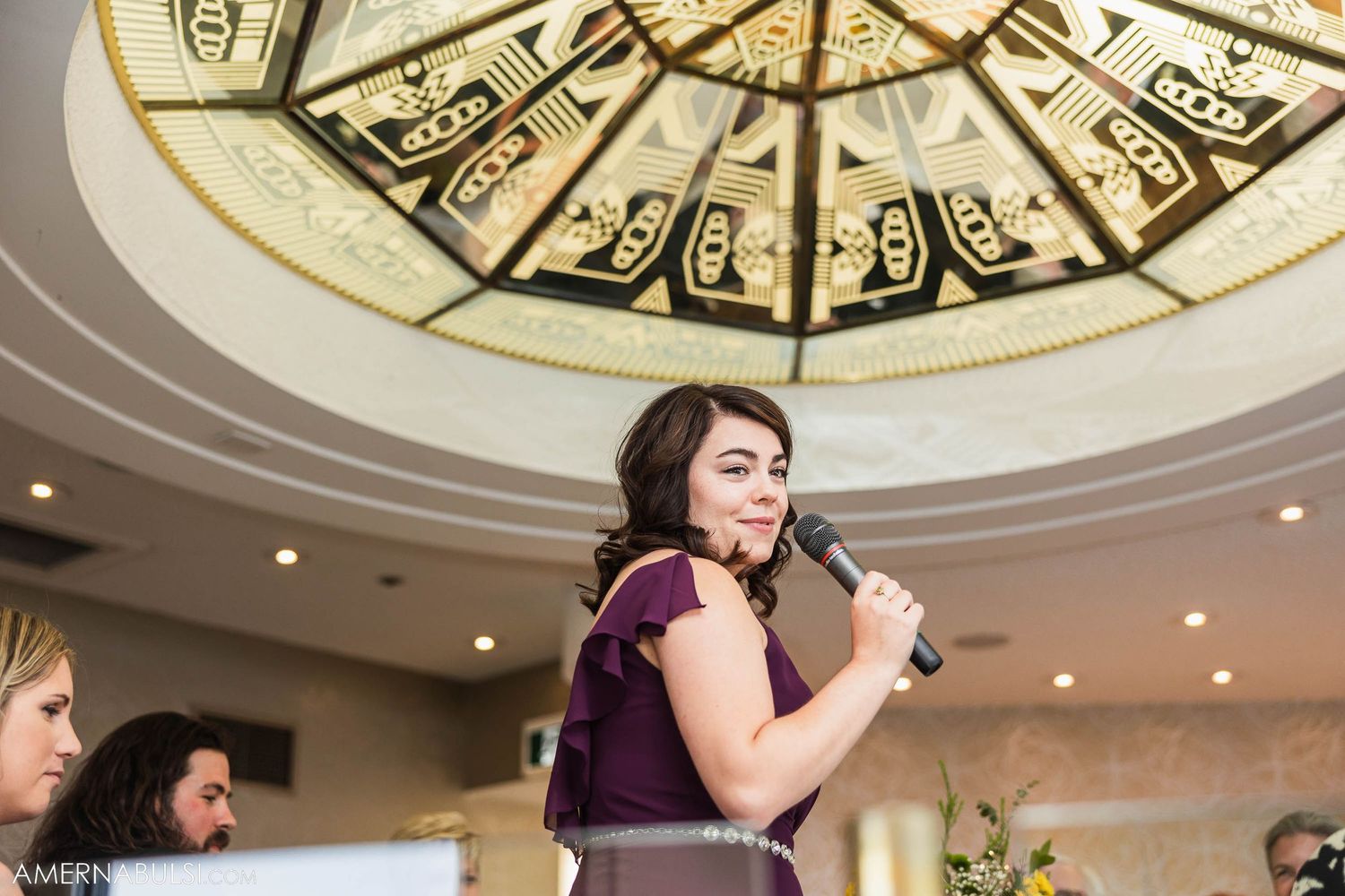 Speaker delivering speech under decorative domed ceiling at formal event.
