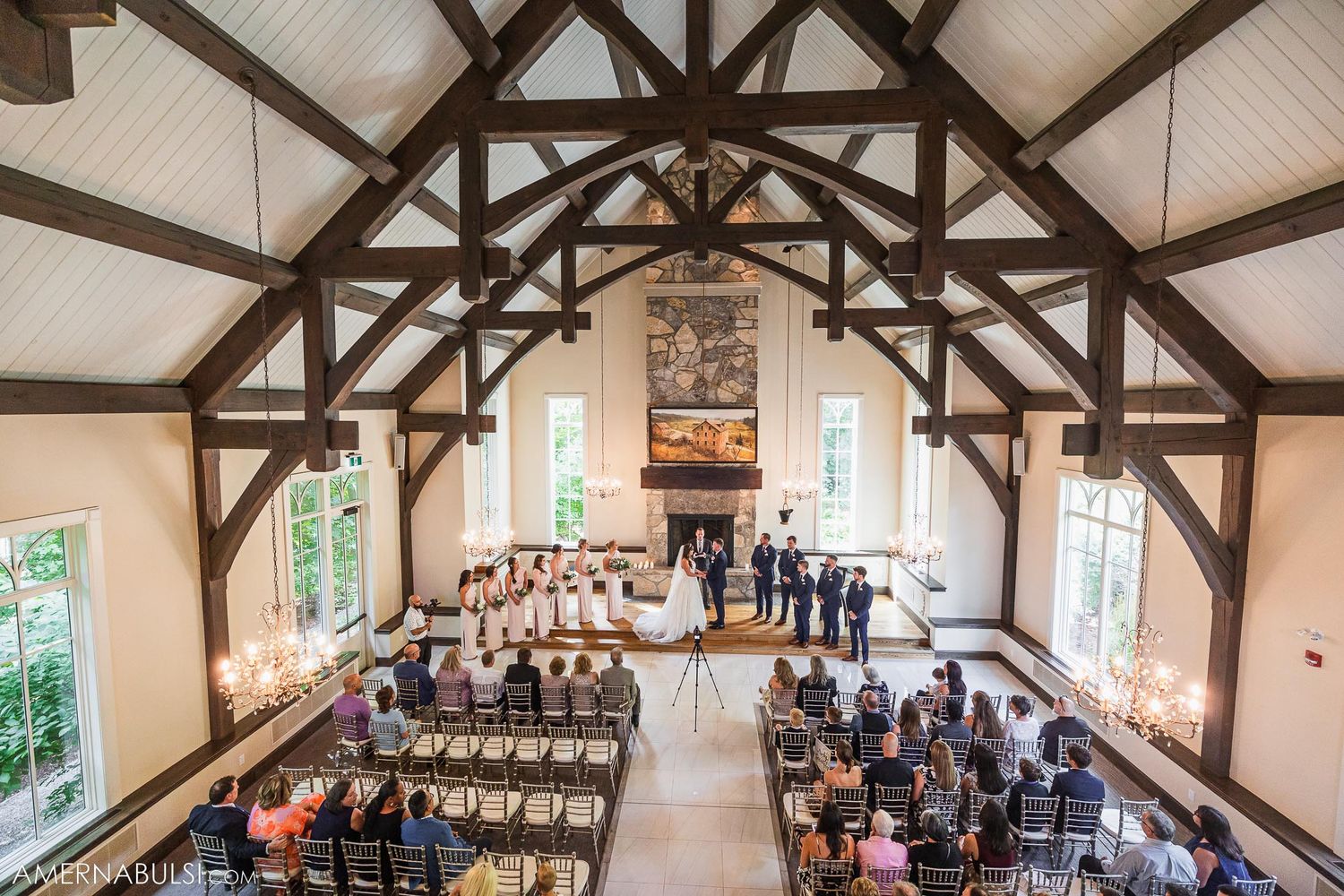 Aerial view of wedding ceremony in progress inside chapel with wooden trusses and white chairs.