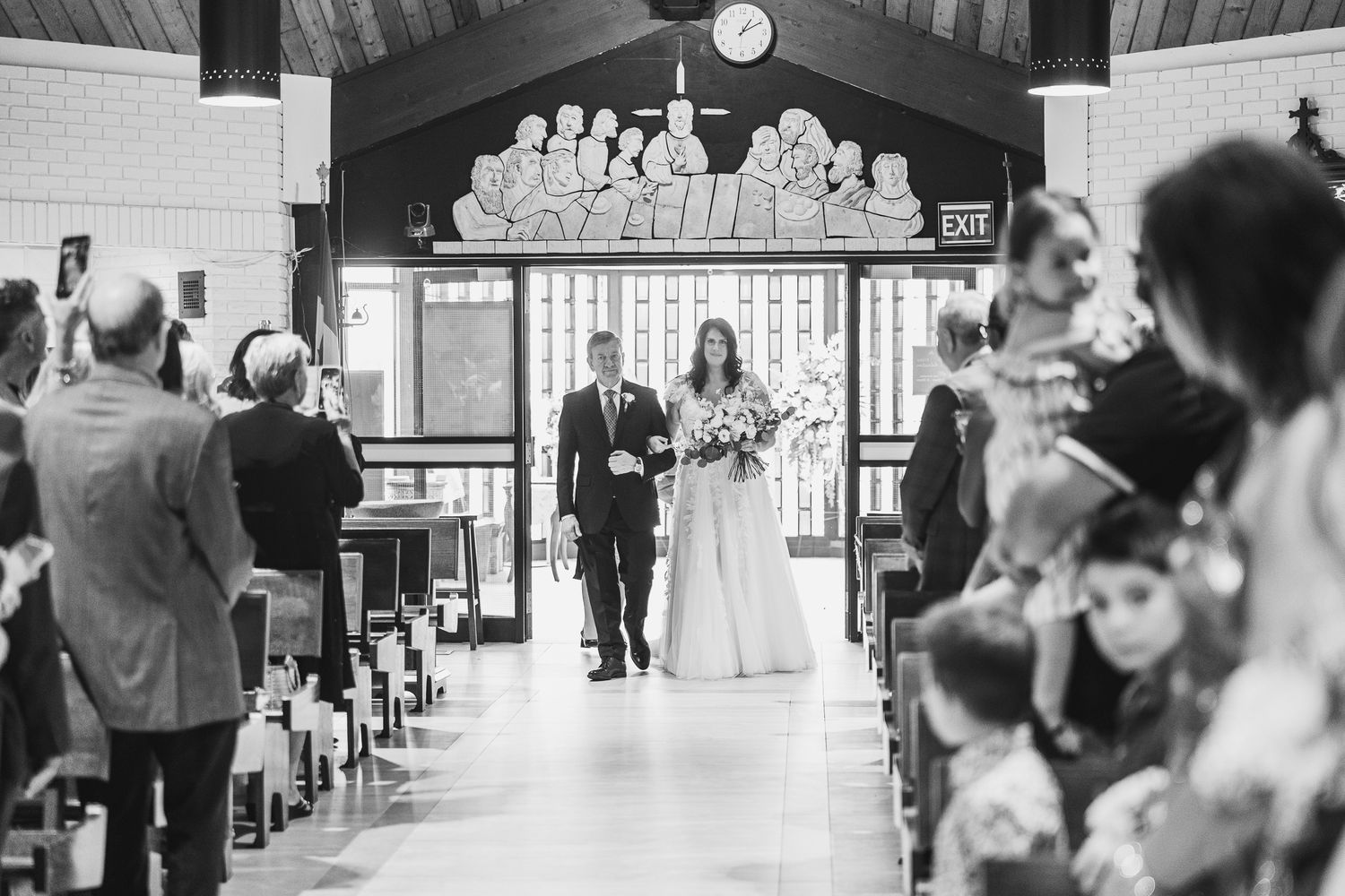 Bride walks down the church aisle in a white gown escorted by her father during a wedding ceremony.