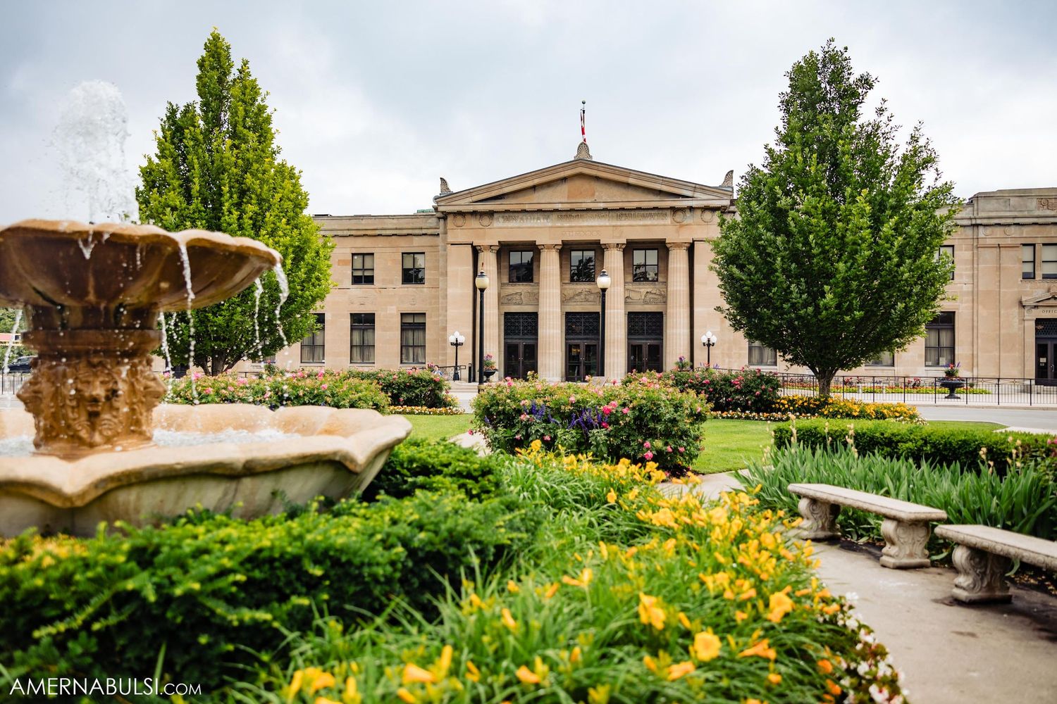 A stately building with classical architecture surrounded by manicured gardens and yellow flowers.
