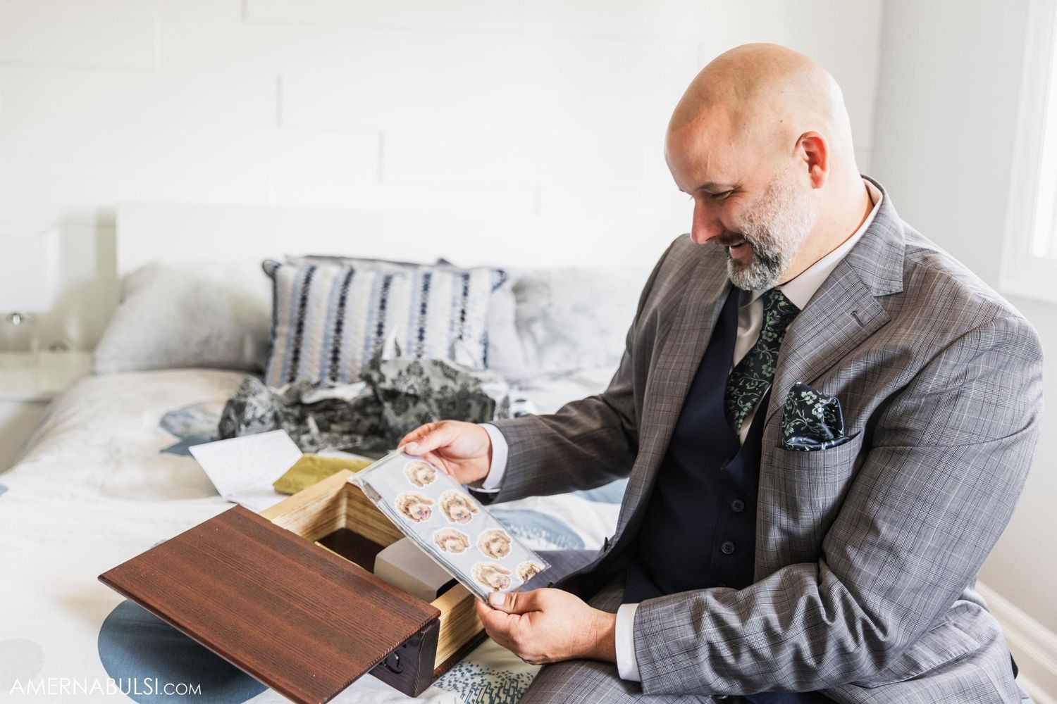 Person in grey suit reading a letter while sitting on bed.