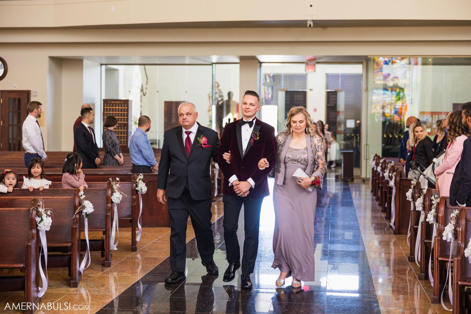 Wedding party walking down church aisle with polished floors and wooden pews.