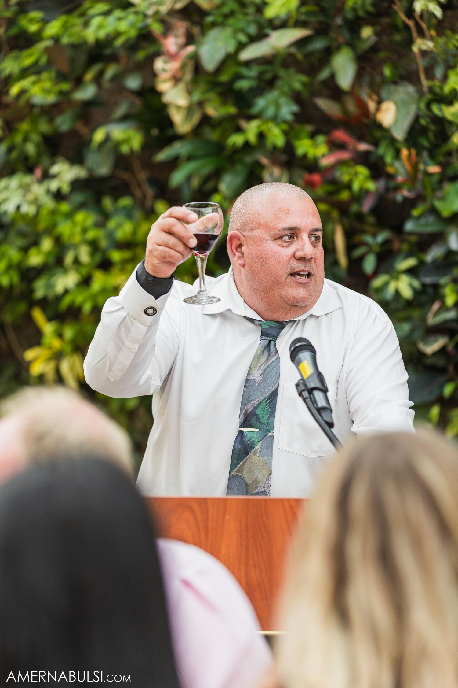 A person in white raises a glass during a wedding toast at an outdoor reception.