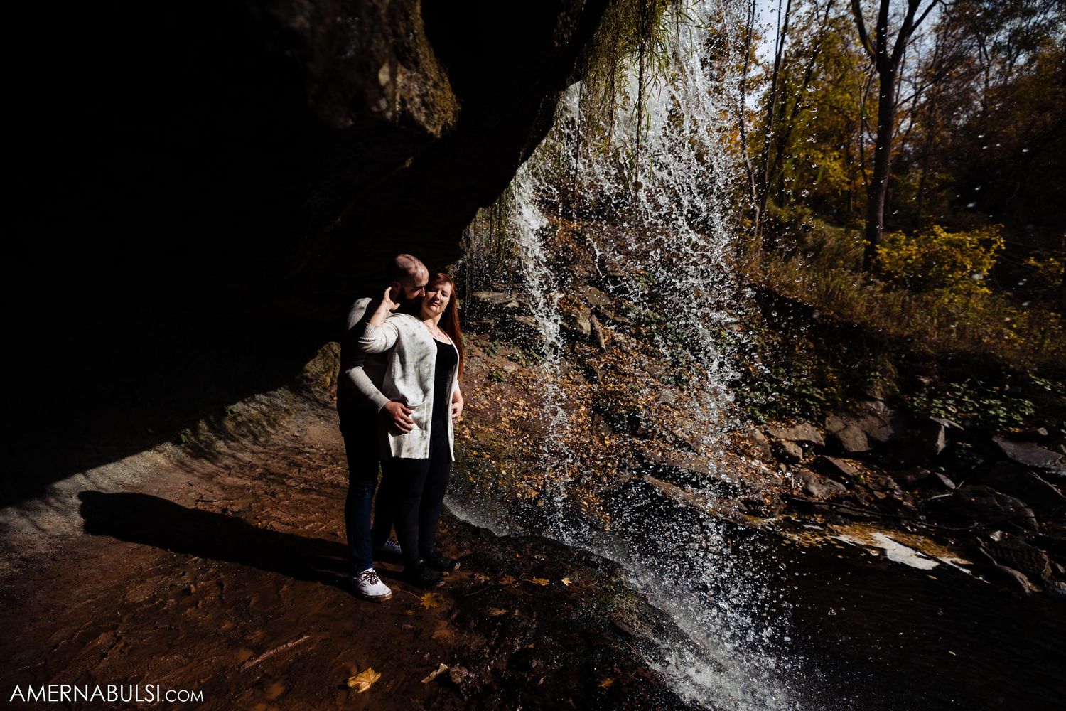Silhouettes standing under cave opening with cascading waterfall.