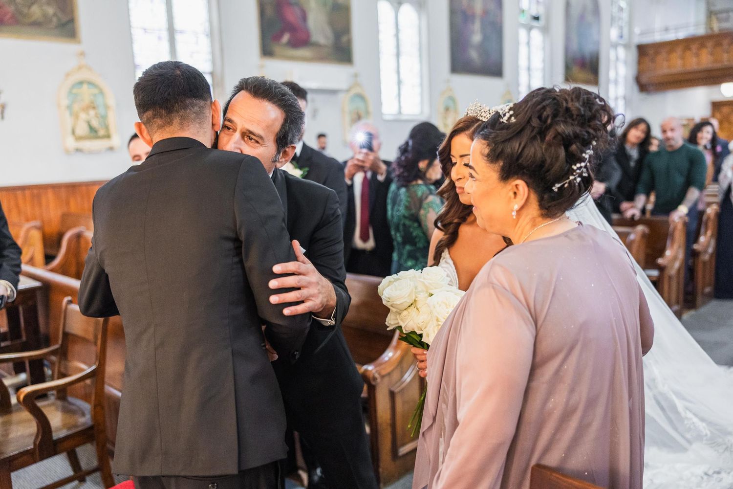 Wedding guests share emotional embraces during the ceremony in a traditional church setting.