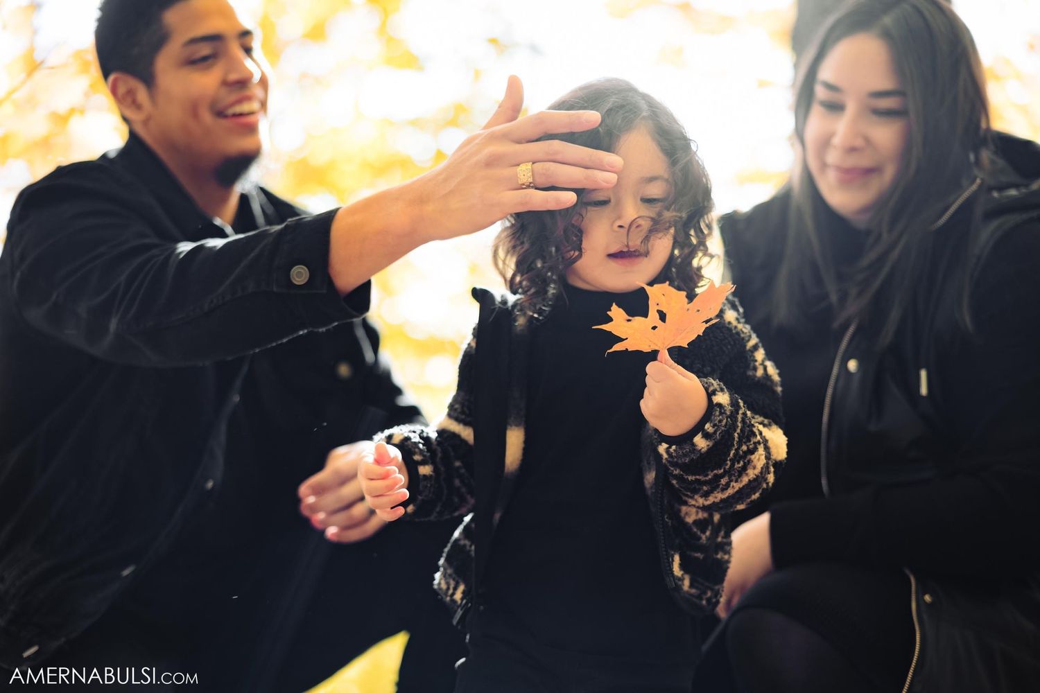 A family plays with falling autumn leaves during an outdoor photo session.
