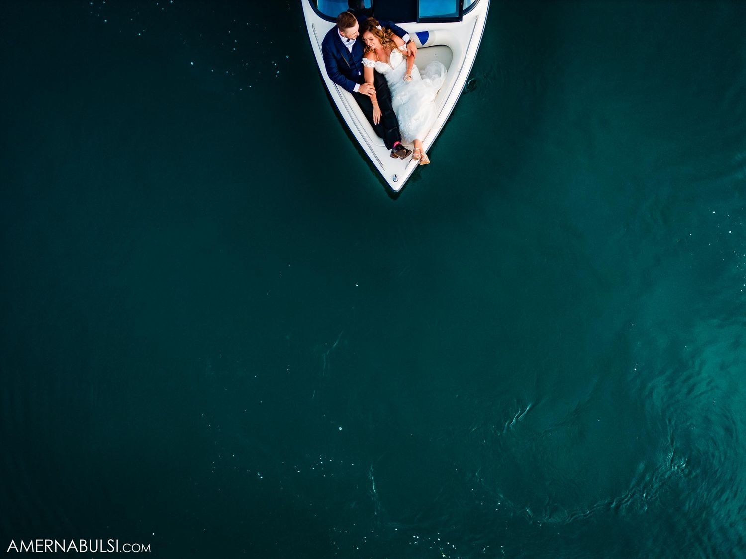 Aerial view of a couple in a small white boat on deep turquoise waters.