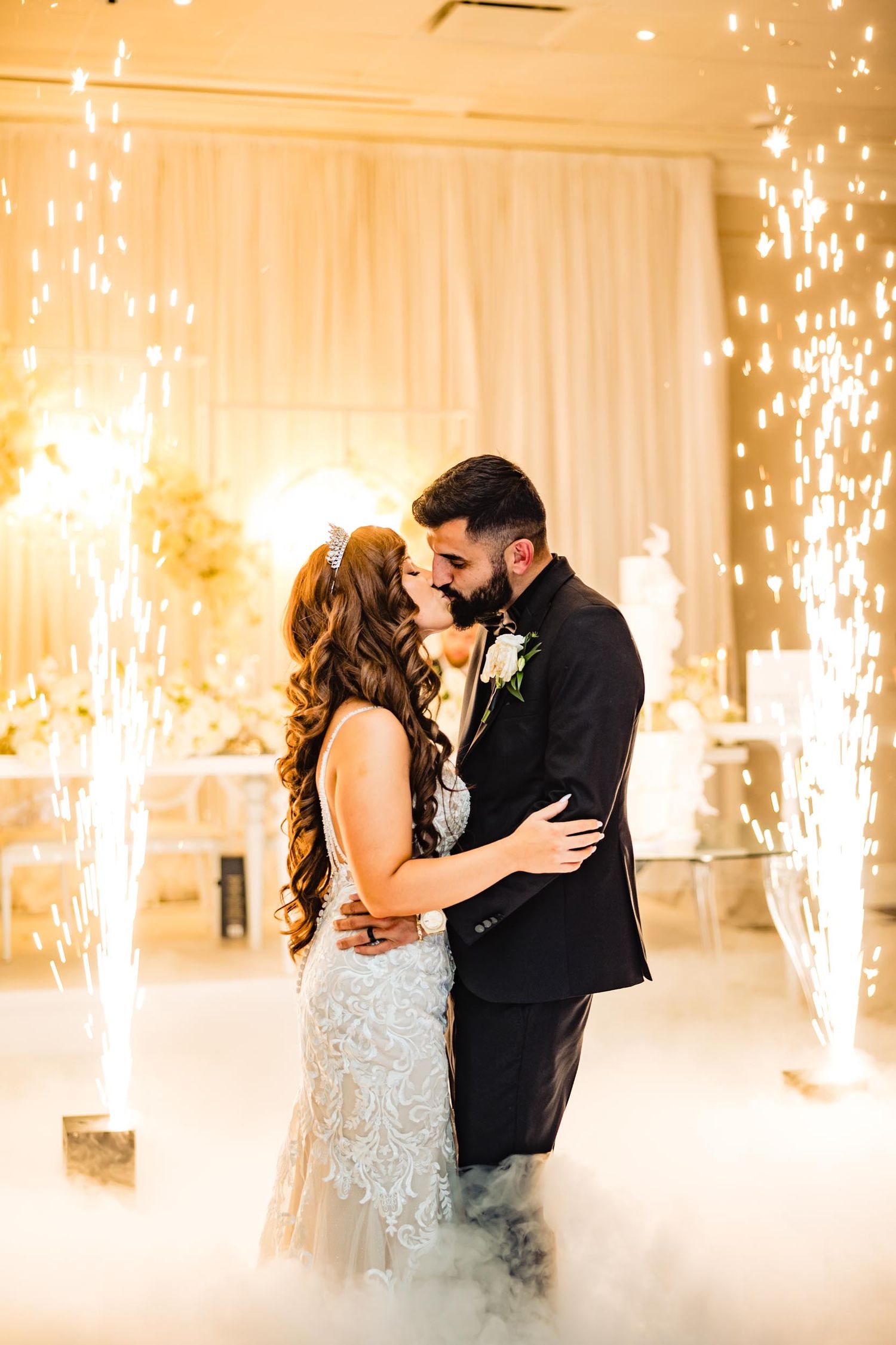 Romantic first dance with sparklers and fog effects in an elegant white reception venue.