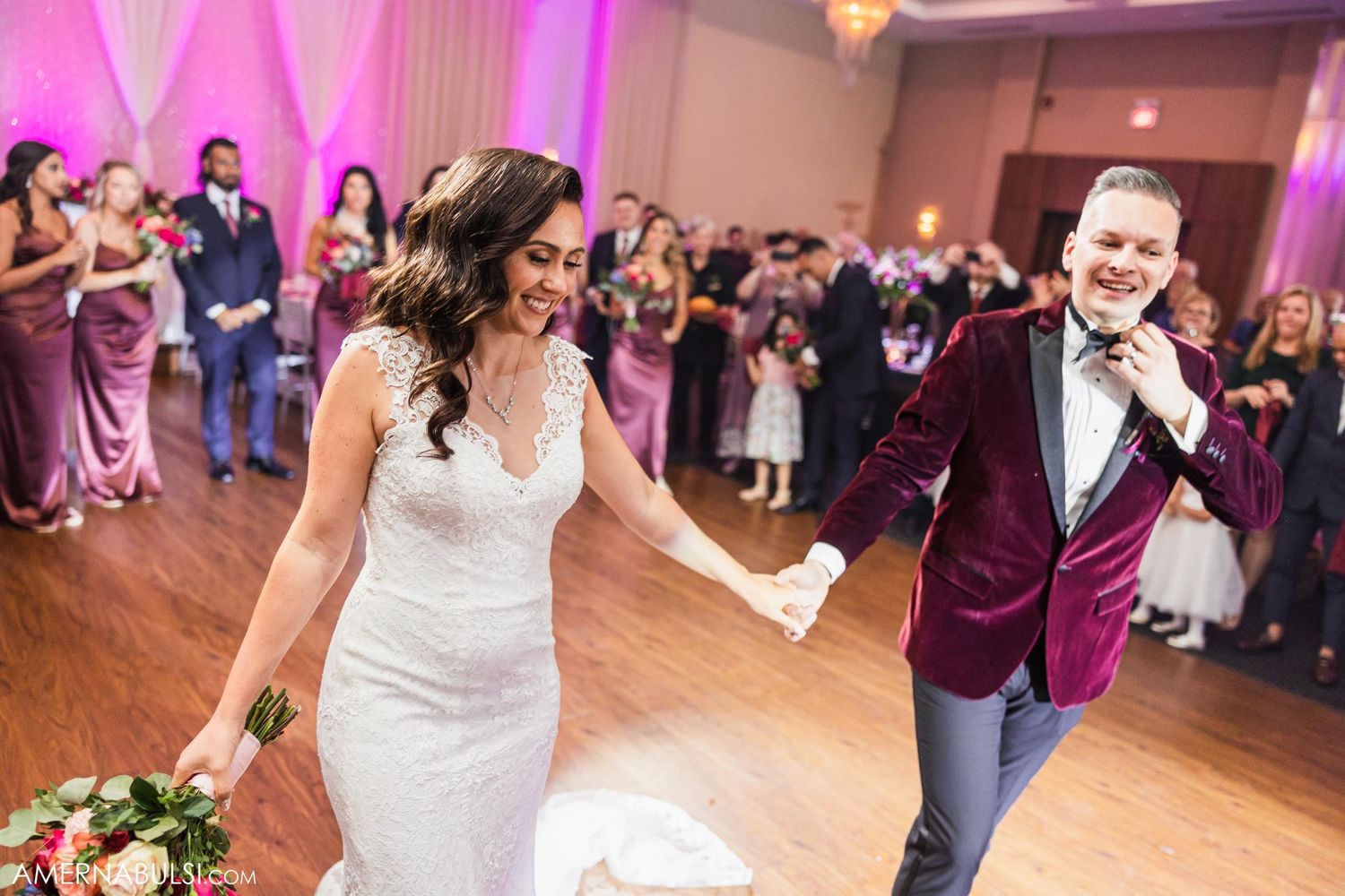 Wedding couple dancing during their reception with pink lighting and guests watching from the sides.