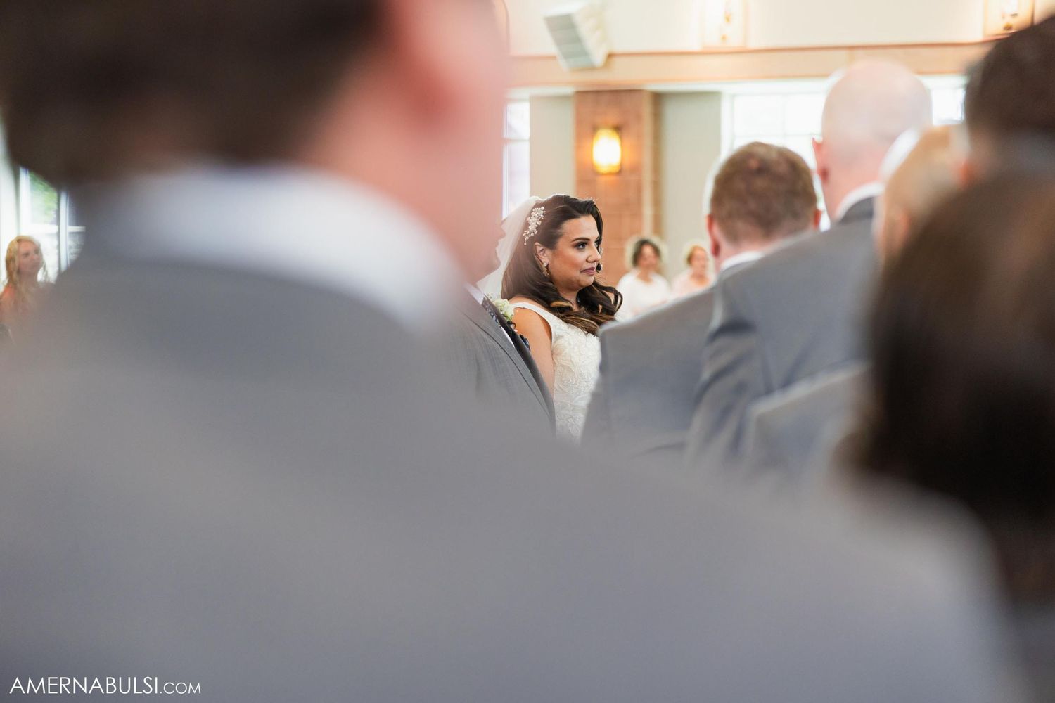 A glimpse of a bride through wedding guests during a church ceremony.