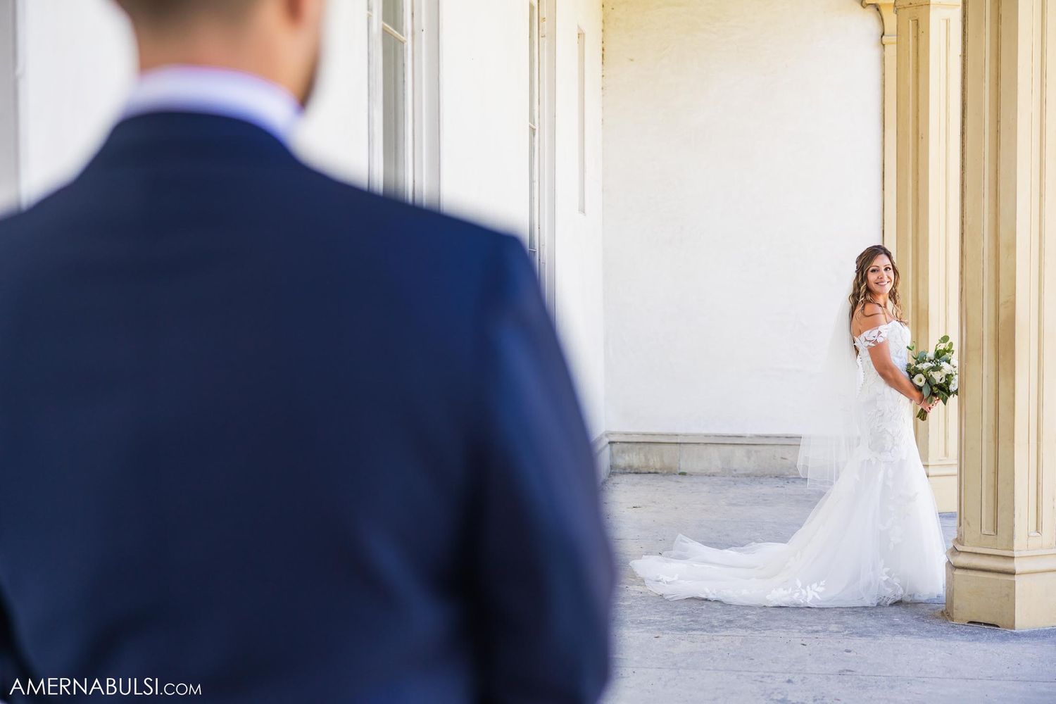 First look wedding scene with flowing white dress against classical columns.