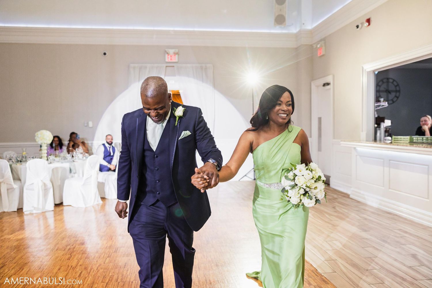 Wedding party members in formal attire walking through reception venue hand in hand.