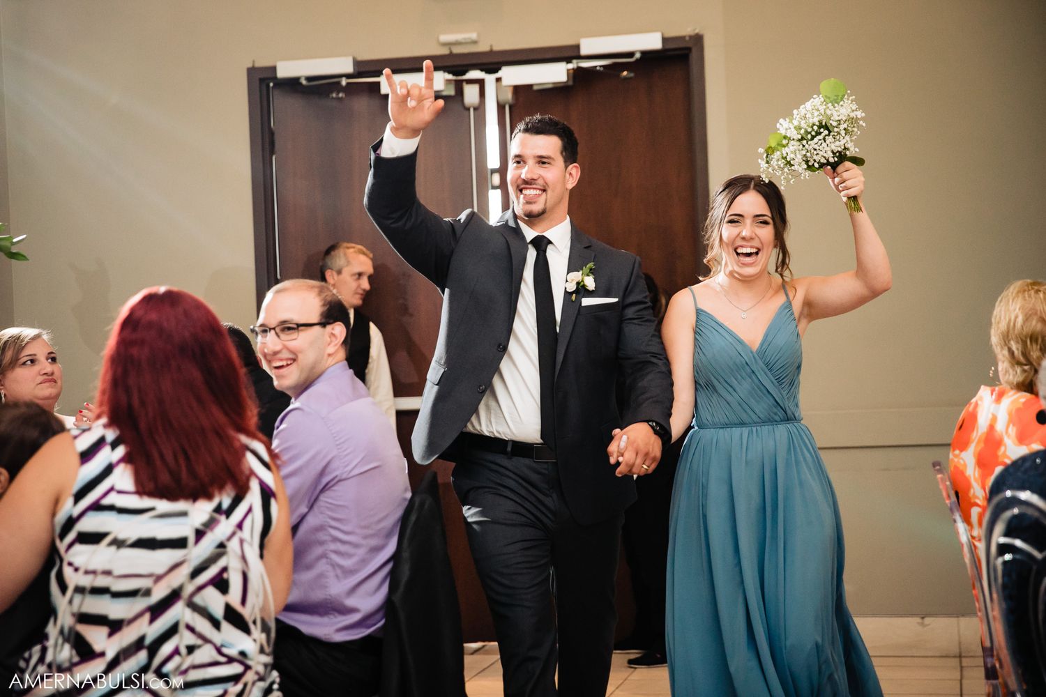 Wedding party members make their grand entrance at the reception with raised arms.