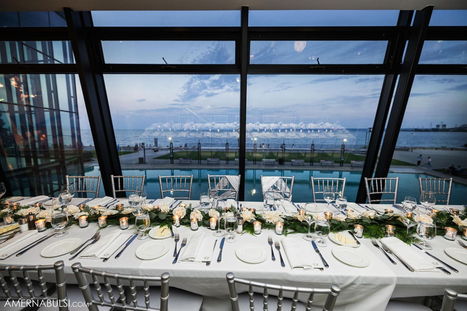 Elegant wedding reception table setup overlooking a waterfront view through large windows.