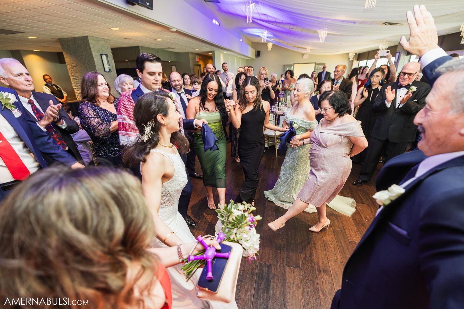 Wedding guests dance and celebrate during lively reception party on wooden dance floor.