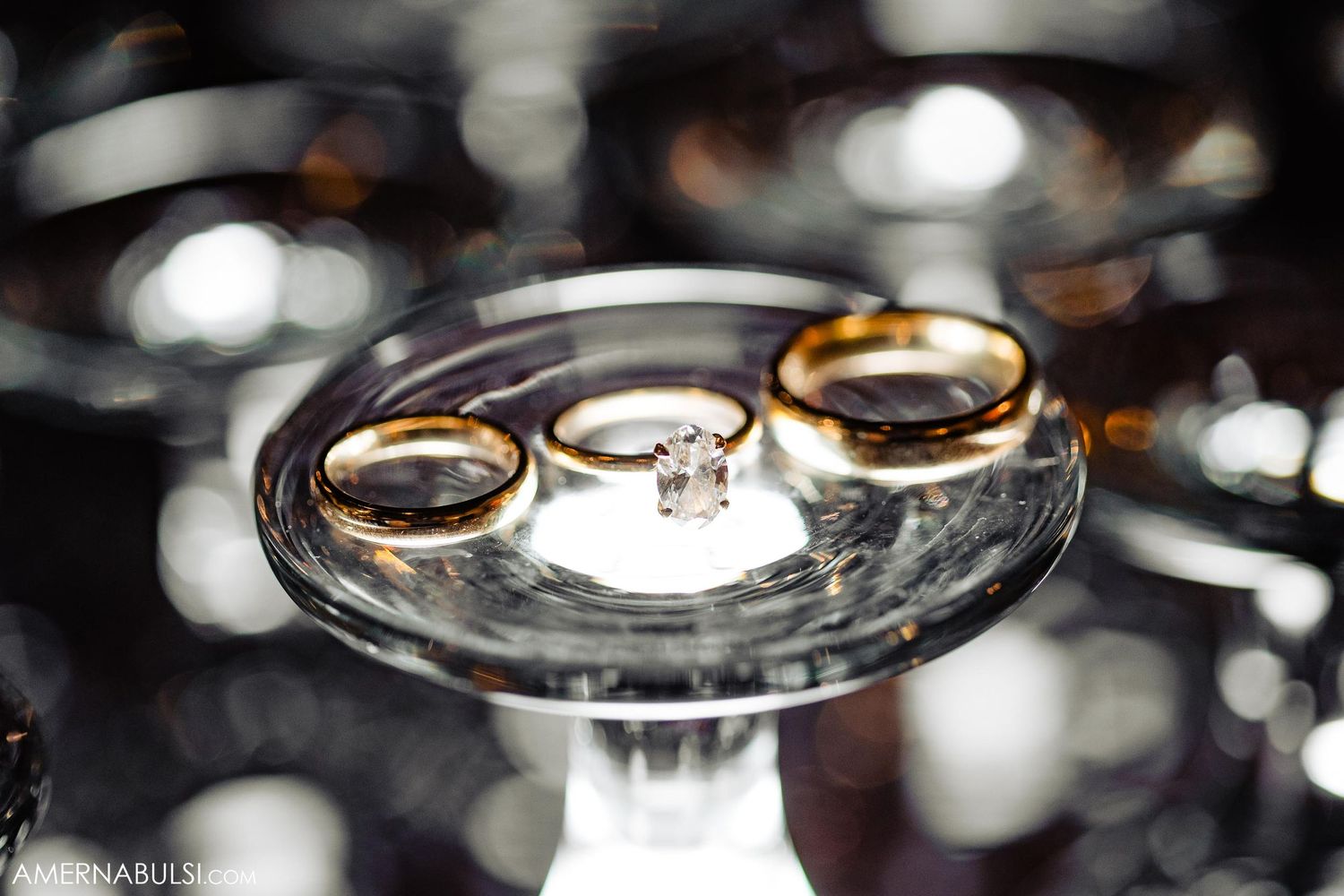 Wedding rings displayed on a crystal glass pedestal with bokeh lighting effects in the background.
