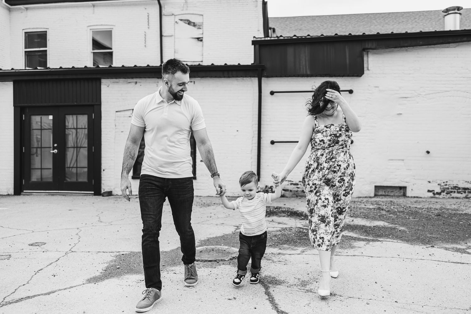 Casual family walking and holding hands against white brick wall in black and white.