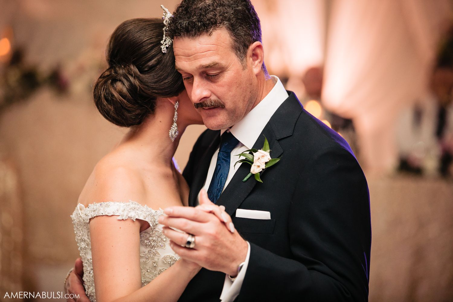 Newlyweds share emotional first dance at elegant wedding reception with romantic lighting.