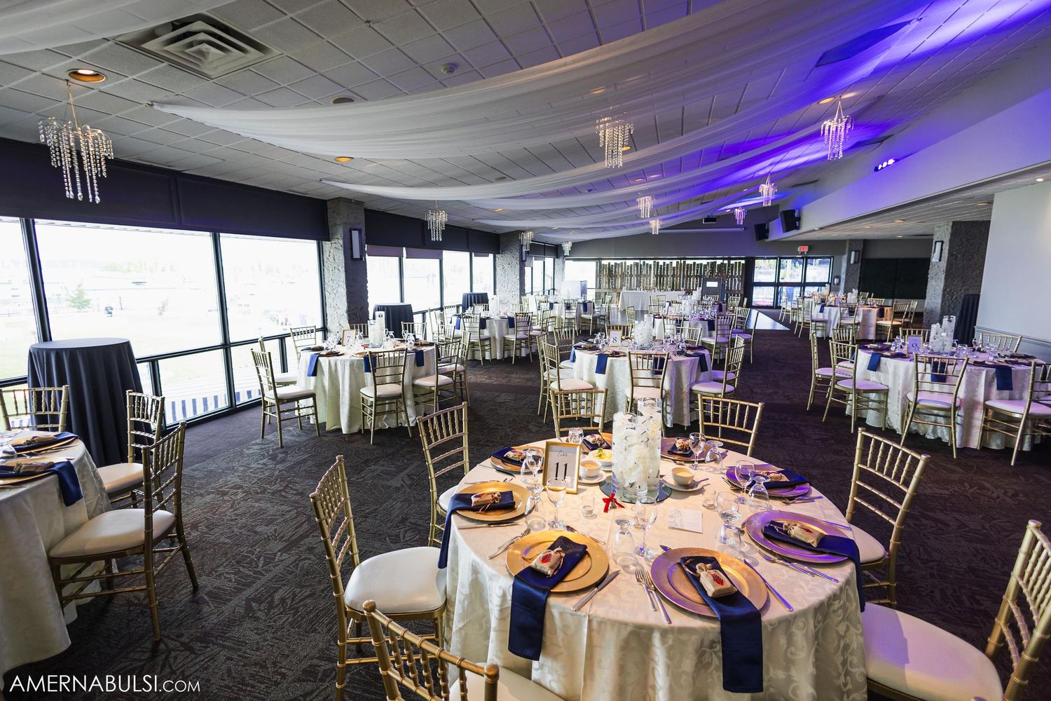 Modern wedding reception venue with purple lighting and round tables set for dinner.