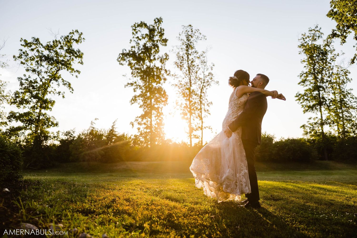 Newlyweds dance in a sunlit field during golden hour with trees in the background.