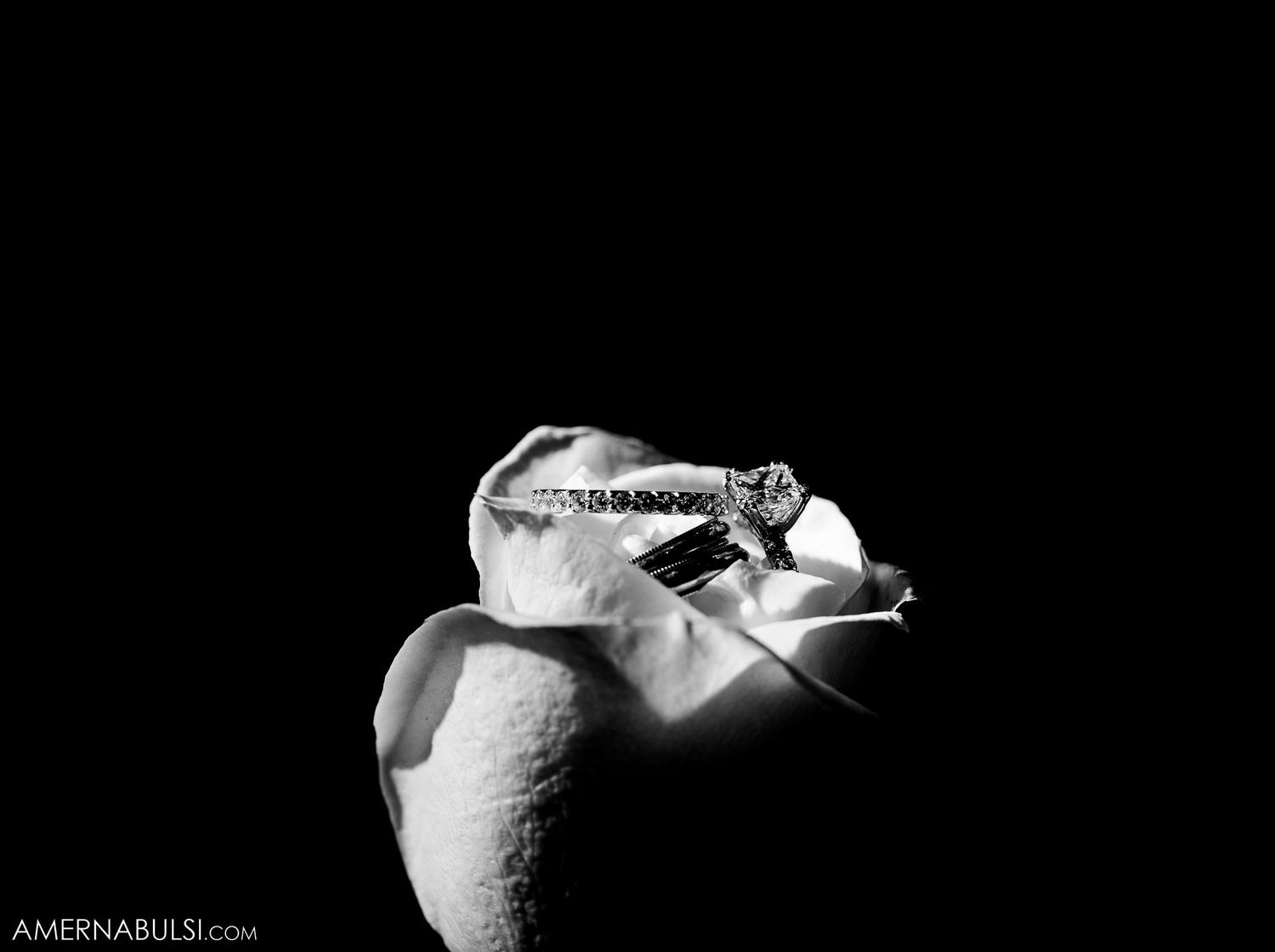 Close-up black and white photo of wedding rings on textured surface.
