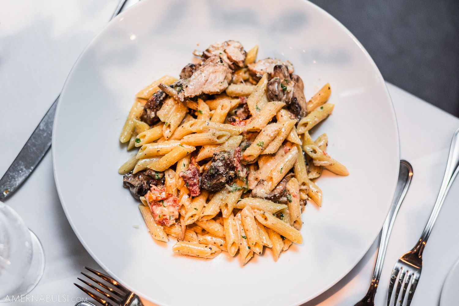 Creamy pasta dish with mushrooms and herbs served on a white plate with silverware.