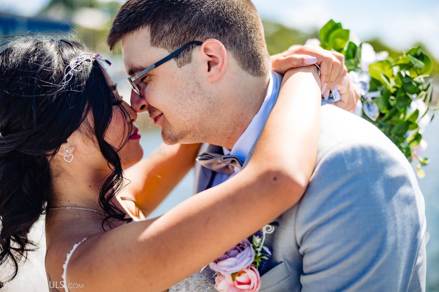 A romantic wedding moment outdoors with light blue attire and pink floral bouquet details.