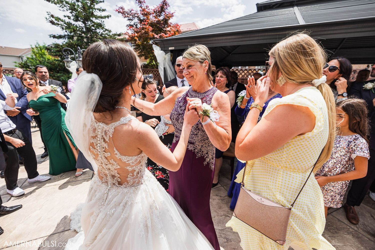 Wedding guests dancing and celebrating at an outdoor reception on a sunny afternoon.