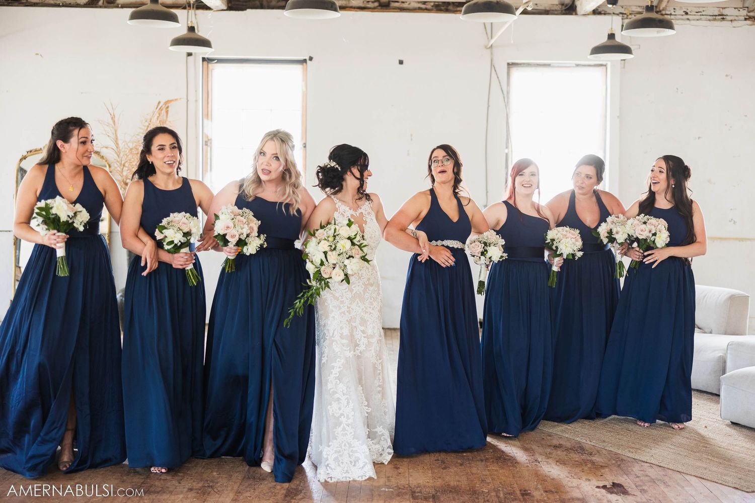 Wedding party poses together in navy and white dresses against white walls and windows.
