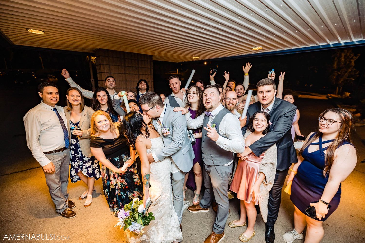 A celebratory group photo of wedding guests posing together in a dimly lit indoor venue.