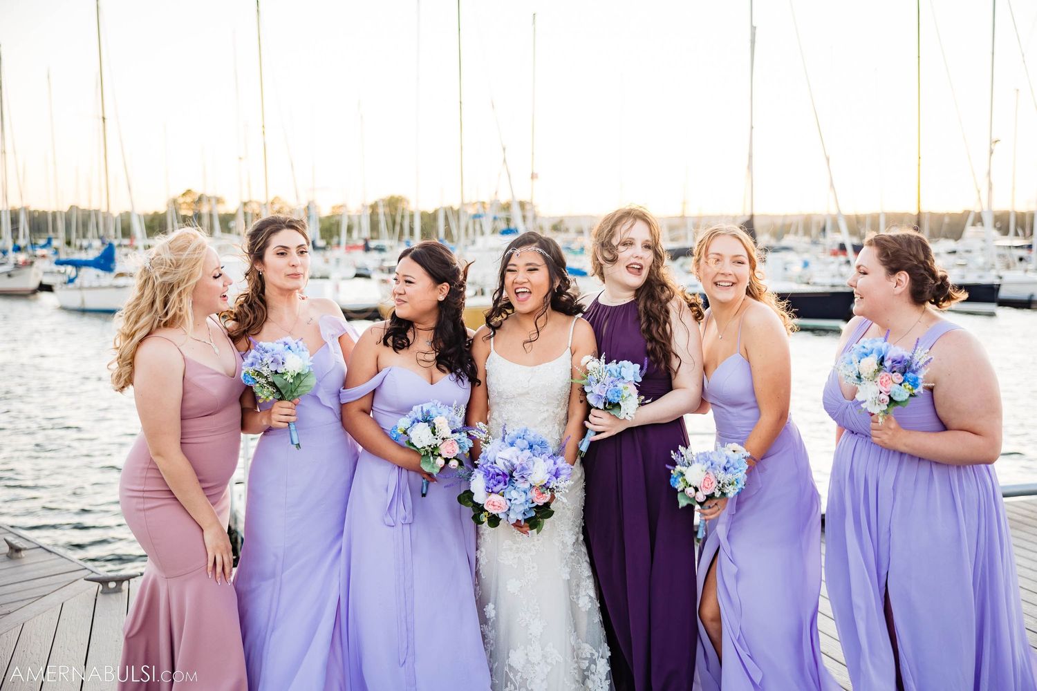 Wedding party with floral bouquets smiling together on wooden dock by marina.